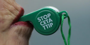 Eine Frau hält im Mund eine Trillerpfeife. Darauf steht „Stopp Ceta TTIP“