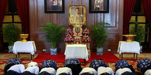 Menschen knien vor einem Bild von Thailands König Bhumibol