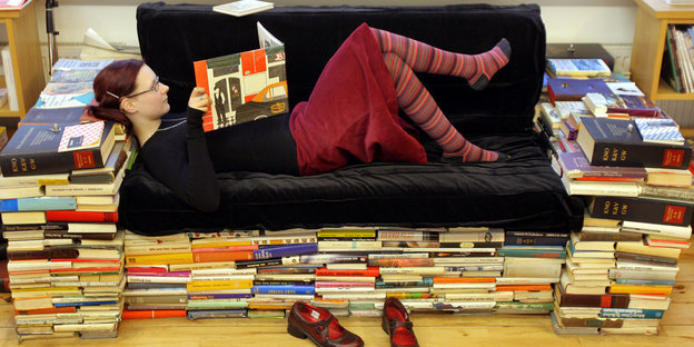 Eine Frau liest auf einer Couch liegend ein Buch