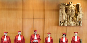sechs Menschen in roten Roben, darüber ein Adler aus Holz