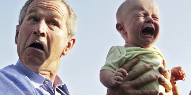 George W. Bush verzieht das Gesicht während er ein schreiendes Baby hält