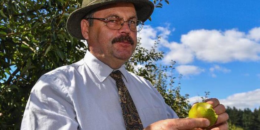 Hiilmar Schwärzel von der Obstbauversuchsstation in Müncheberg (Brandenburg) steht vor einem Apfelbaum, trägt einen Hut und hält einen Apfel in der Hand