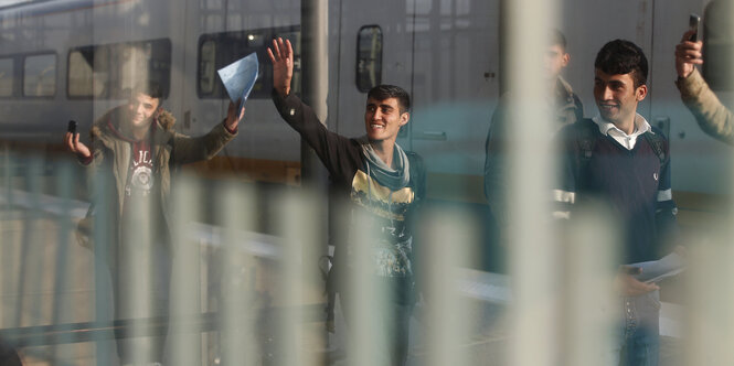 Ein paar Jungen stehen an einem Bahnsteig vor einem Zug und winken, dabei lachen sie