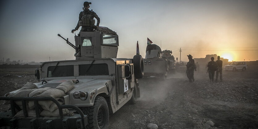 Rechts im Hintergrund die aufgehende Sonne, im Vordergrund Panzer und bewaffnete Soldaten