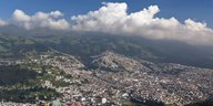 Panorama auf die Stadt Quito, um sie herum weite grüne Flächen, der Himmel ist blau und teils mit großen weißen Wolken bedeckt
