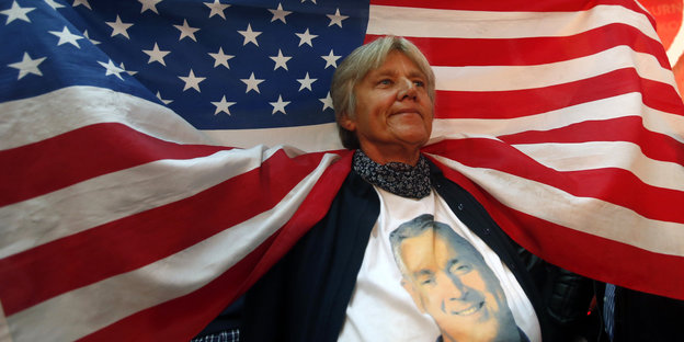 Eine Frau trägt ein T-Shirt mit dem Gesicht Djucanovics und hält eine US-Fahne in die Höhe, die über ihre Schultern fällt