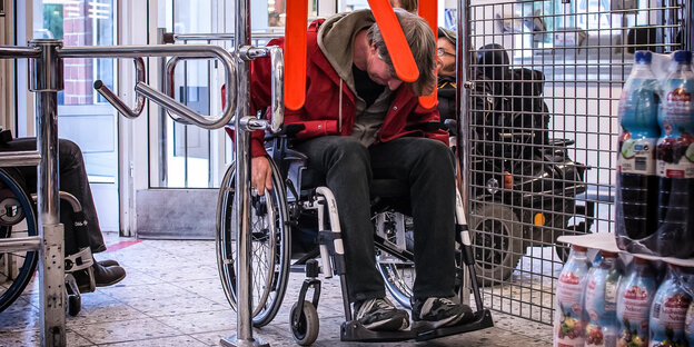 Ein Mann passiert im Rollstuhl eine Einkaufswagen-Schranke in einem Supermarkt
