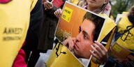 Ein Schild mit dem Foto eines Mannes wird von einer Frau in gelber Weste in den Händen gehalten