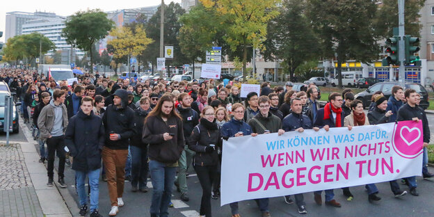 Eine Menschenmenge zieht durch eine Straße, die Menschen in der ersten Reihe tragen ein Banner mit der Aufschrift "Wir können was dafür wenn wir nichts dagegen tun"