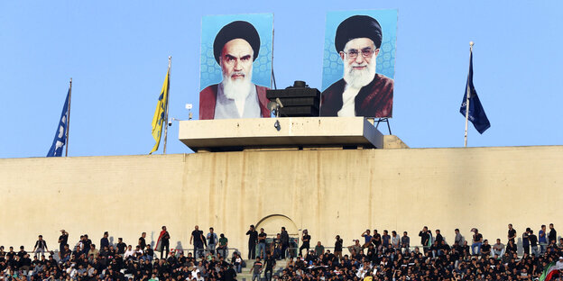 Porträts von Ayatollah Khomeini (links) und Ayatollah Ali Khamenei hängen über einer Mauer, darunter eine Menschenmenge