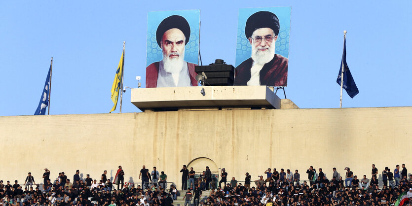 Porträts von Ayatollah Khomeini (links) und Ayatollah Ali Khamenei hängen über einer Mauer, darunter eine Menschenmenge