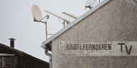 Auf einem Haus mit Satellitenschüsseln steht "Kabelfernsehen TV"
