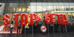 große Buchstaben "Stop Ceta" vor einem Gebäude mit viel Glas