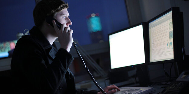 Ein junger Mann sitzt vor einem PC und telefoniert