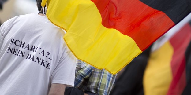 Ein Mann von hinten mit Deutschlandfahne, auf seinem Shirt steht „Scharia nein danke“