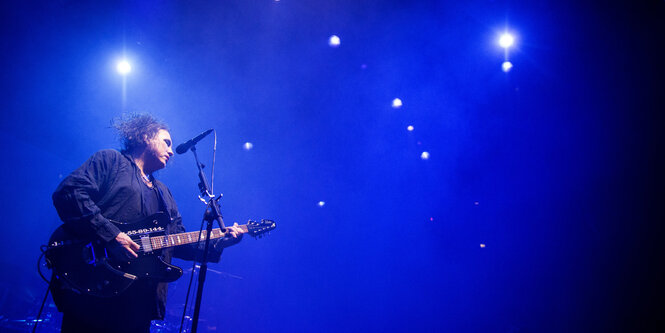 Robert E. Smith spielt Guitarre, das Licht ist blau, Spots blitzen