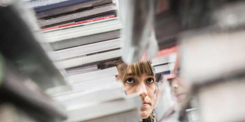 Eine Frau guckt durch mehrere Bücherstapel hindurch