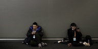 Zwei Jungen sitzen an eine graue Wand gelehnt und spielen mit ihren Smartphones