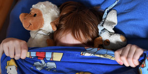 Ein Kind zieht sich eine blaue Bettdecke über das Gesicht