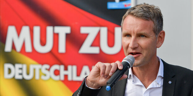 Björn Höcke spricht in ein Mikrofon, hinter ihm ist eine Deutschlandfahne zu sehen, auf der „Mut zu Deutschland“ steht