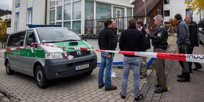 ein Polizeifahrzeug und eine Gruppe von Ermittlern hinter rot-weißem Flatterband