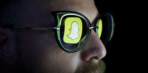 Ein Mann mit einer Sonnenbrille, in der sich das Snapchat-Logo spiegelt