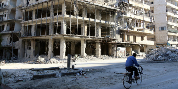 Ein Mann fährt mit einem Fahrrad an einem völlig ausgebombten Haus in Aleppo vorbei