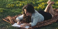 Eine junge Frau liegt bäuchlings auf einer Wiese und schreibt etwas