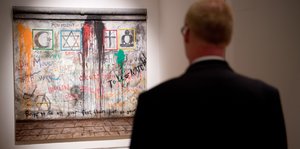 Mann steht vor einem Bild der Berliner Mauer
