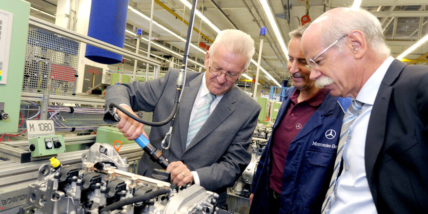 Kretschmann schraubt an einem Motor, Zetsche schaut zu