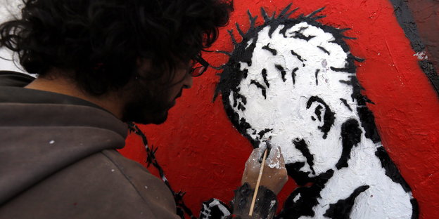 Ein Künstler malt ein Kind in einem Sarg an die Wand