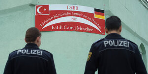 Zwei Polizisten stehen mit dem Rücken zum Betrachter vor der Mauer einer Moschee