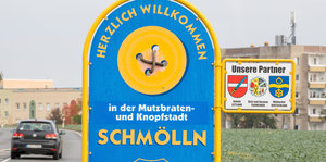 Schild an Straße, Aufschrift "Herzlich willkommen in der Mutzbraten- und Knopfstadt Schmölln"