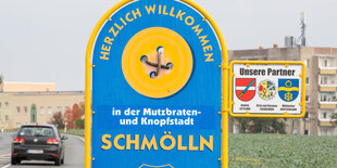 Schild an Straße, Aufschrift "Herzlich willkommen in der Mutzbraten- und Knopfstadt Schmölln"