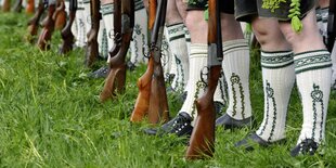 Männerbeine in bestickten Traditionssocken, davor stehen Gewehr