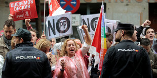 Menschen mit Plakaten werden von Polizisten bewacht