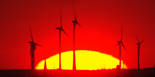 Vor dem rotgefärbten Himmel und der untergehenden Sonne sind Windräder zu erkennen