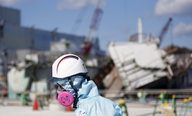 Ein Arbeiter mit Helm und Schutzmaske vor einer Ruine