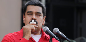 Nicolas Maduro, im roten Hemd, küsst ein Kreuz