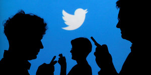 Mehrere Menschen verschattet vor einem blauen Screen, darauf der weiße Twitter-Vogel