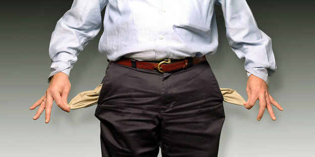 Ein Mann in Anzughose und Hemd zieht seine leeren Hosentaschen nach außen