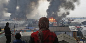 Menschen schauen auf die Rauchwolken und Flammen über dem Flüchtlingslager von Calais