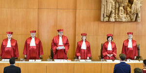 Sechs Richter in roten Roben stehen hinter ihrem Tisch und schauen die Zuschauer an
