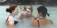 Frauen baden in einer blauen Lagune und tragen weiße Gesichtsmasken