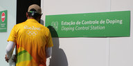 Ein Helfer im gelben Shirt geht auf eine Tür zu, daneben hängt ein Schild mit der Aufschrift: Dopingkontrolle