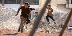 Vier junge Männer von Fateh-al-Scham rennen in gebückter Haltung durch die Trümmer Aleppos