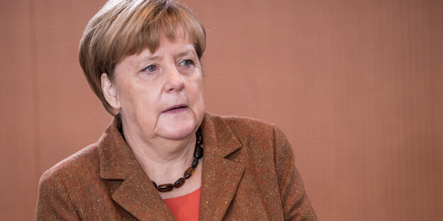 Angela Merkel trägt braun und steht vor einer braunen Wand
