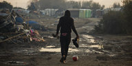 Ein Mann geht auf schlammig-sandigem Weg durch das verwüstete Camp