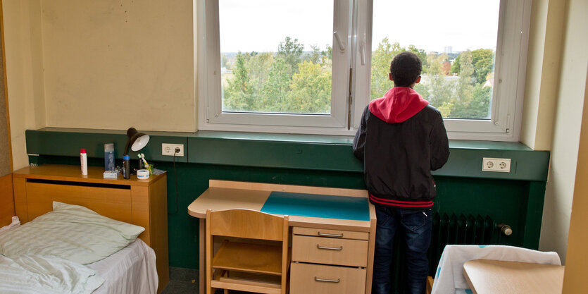 Junge steht am Fenster eines Wohnheimzimmers