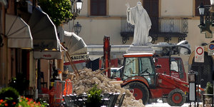 Eine Straße in einer italienischen Stadt mit Cafés, mittendrin ein Trümmerberg